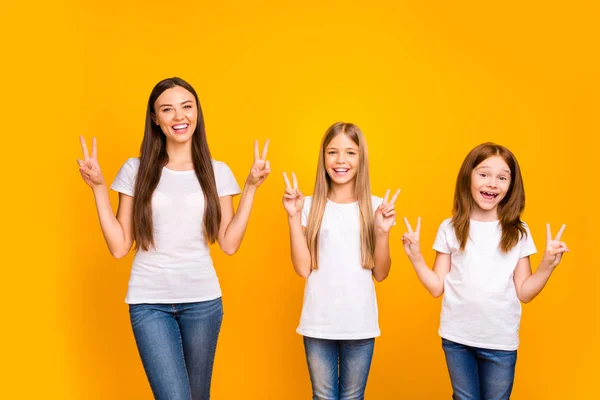 Krásné tři sesterské dámy v kladné náladě zobrazující v-symboly, nosí neformální oblečení izolované žluté pozadí — Stock fotografie