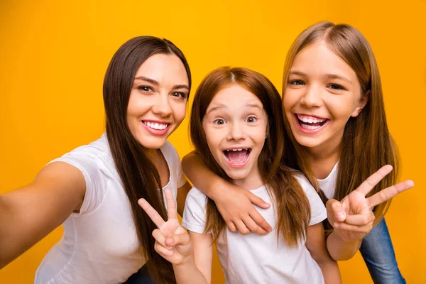 Foto de tres hermanas haciendo selfies mostrando símbolo de v-signo usar camisetas blancas casuales fondo amarillo aislado —  Fotos de Stock