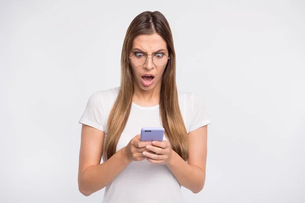 Nerveuze dame houden telefoon in handen niet geloven wat lezing slijtage specs en casual t-shirt geïsoleerd witte achtergrond — Stockfoto