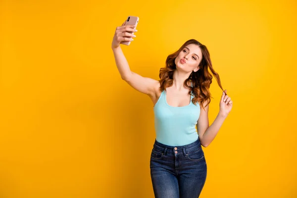 Фото женщины, держащей телефон, делающей фотографии с кокетными поцелуями носят топ и джинсы на изолированном желтом фоне — стоковое фото