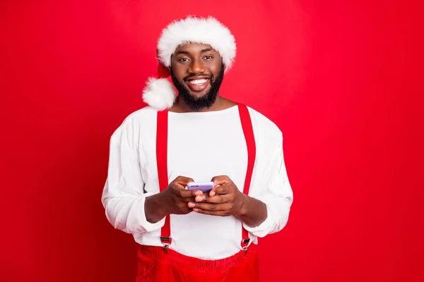 Retrato de alegre santa claus negro en sombrero de Navidad usando gadget de teléfono celular leer mensajes de año nuevo con suéter blanco aislado sobre fondo rojo —  Fotos de Stock