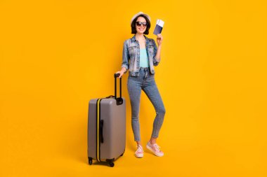Full length body size photo of toothily smiling cheerful glad cute attractive nice girlfriend wearing jeans denim jacket rejoicing with being able to go abroad while isolated with yellow background clipart