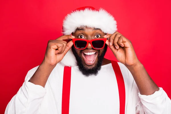 Close up foto de Papai Noel Africano espantado tocando suas especificações gritando wow omg ver milagre noel vestindo elegante suéter branco isolado sobre fundo vermelho — Fotografia de Stock
