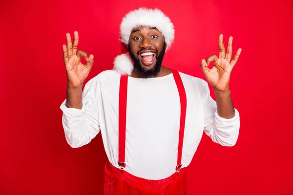 Portrét veselého černého Santa Clause ukazující ok nápis křičící nošení čepice bílý svetr izolovaný přes červené pozadí — Stock fotografie