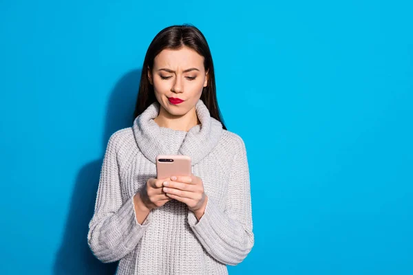 예쁜 여자 들고 전화 손 에 대한 의심 남자 친구 sms 착용 따뜻한 니트 풀오버 고립 된 파란색 배경 — 스톡 사진