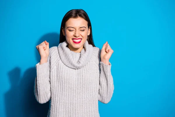 Portrait of cheerful girl closing her eyes raising fists wearing grey jumper isolated over blue background — Stok fotoğraf