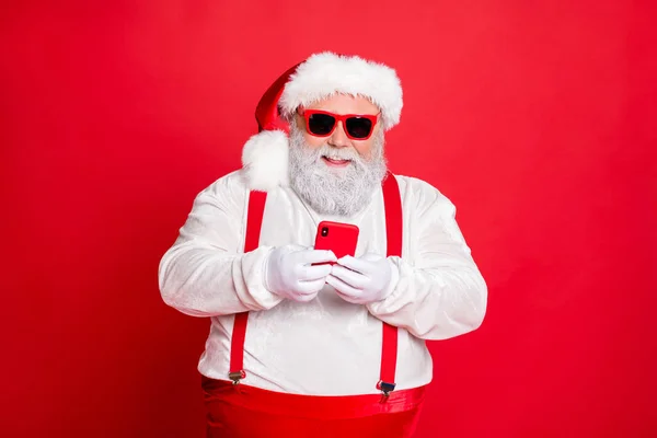 Portret van grappige funky Fat overgewicht Santa Claus met grote buik buik gebruik mobiele telefoon commentaar Nieuwjaar Posts dragen stijlvolle trendy brillen brillen hoed lezing nieuws geïsoleerd over rode achtergrond — Stockfoto