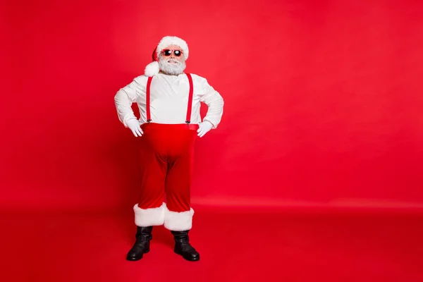 Volledige lichaam foto van positieve grappige vet overgewicht Santa Claus met stijl brillen grote buik klaar om te vieren Nieuwjaar partij permanent geïsoleerd over rode achtergrond dragen broeken broek — Stockfoto