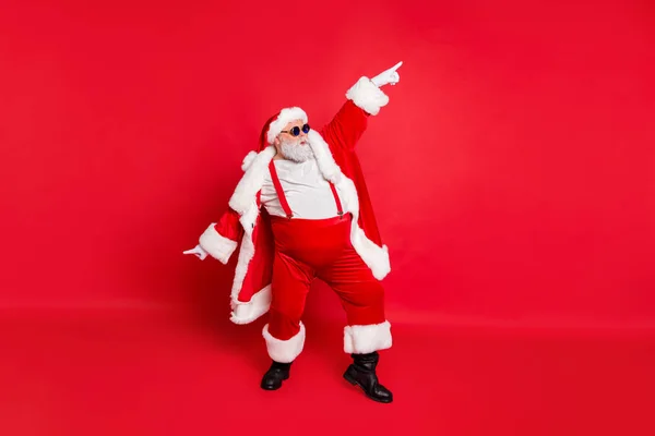 Foto de larga duración de la grasa dabber viejo guapo divertido Santa Claus en gafas de baile con su mano levantada usando estilo elegante pantalones de moda aislados sobre fondo rojo — Foto de Stock