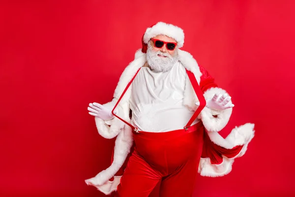 Portrait of style fat overweight santa claus with big funny belly abdomen touch his suspenders overalls posing like a model wearing trousers pants isolated over red background — Stock Photo, Image