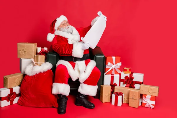 Tipo generoso funky grasa sobrepeso regordeta hombre barbudo de pelo gris sentado en la oficina de correos silla lectura lista de deseos carta envío entrega invierno aislado sobre brillante brillante brillo rojo fondo — Foto de Stock