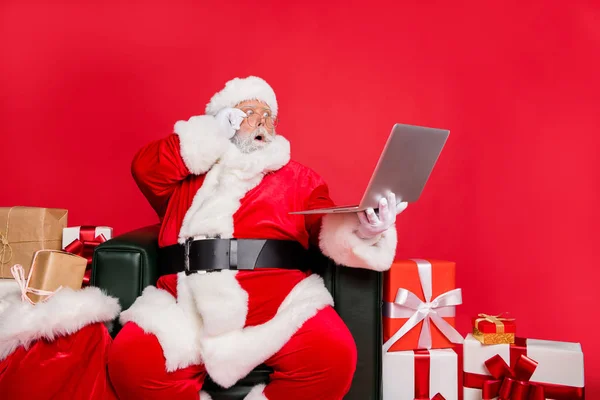 アームチェアショップの配達チェックアドレスリストに座っている驚きの勤勉な脂肪ひげ男セントニコラスは、ウェブ注文妖精の夢のクリスマスタイムは明るい鮮やかな輝く赤い背景に隔離 — ストック写真