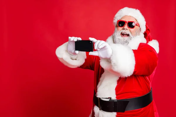 Ritratto di Babbo Natale eccitato in occhiali facendo selfie con dispositivo cellulare sulla vacanza di Natale sorridente indossando cintura isolata su sfondo rosso — Foto Stock