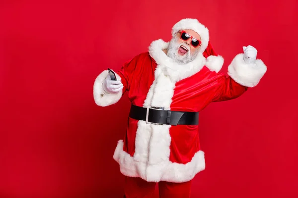 Retrato de Papai Noel louco em chapéu usando dispositivo de telefone celular levantando punhos gritando sim ter festa do ano novo vestindo óculos cinto óculos isolados sobre fundo vermelho — Fotografia de Stock