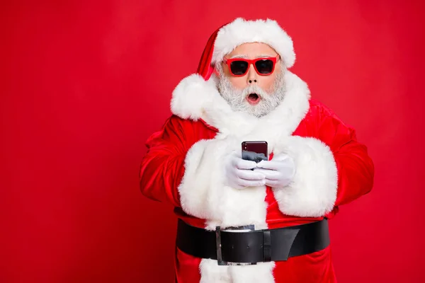 Portrait de père de Noël impressionné dans le chapeau à l'aide d'un appareil de téléphone cellulaire criant omg portant lu sur les événements festifs lunettes ceinture de lunettes isolé sur fond rouge — Photo