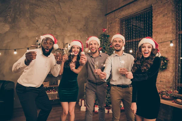 Porträtt av härliga killar damer hålla fyrverkerier glas njuta jultid fira x-mas midnatt bär Santa Claus hatt mössa formella slitage i huset med Noel belysning inomhus — Stockfoto