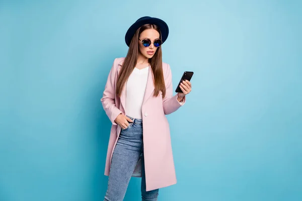 Ritratto di donna stupita utilizzare il suo cellulare leggere notizie meraviglia dire il suo omg indossare abito cappotto rosa elegante jeans jeans occhiali isolati su sfondo di colore blu — Foto Stock