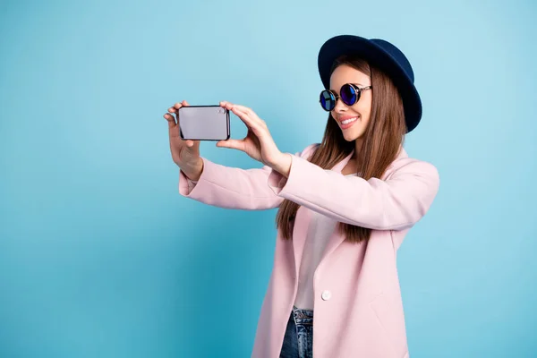 Фотографія з боку профілю веселої дівчини, яка використовує свій мобільний телефон, створюючи портрет, насолоджуючись набережною в рожевому вбранні, ізольованому на синьому фоні — стокове фото