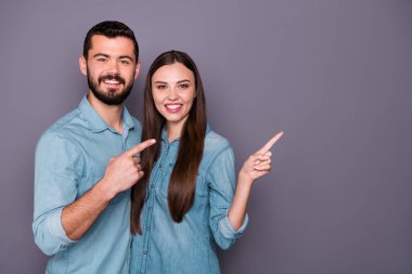 Portrait of two charming people showing adverts with his her fingers wearing denim jeans shirt outfit isolated over grey background clipart