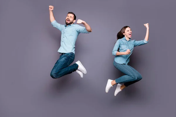Полноразмерная фотография восторженных студентов, прыгающих вверх кулаками и празднующих победу в джинсах, изолированных на заднем плане — стоковое фото