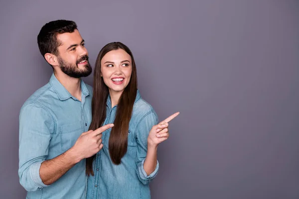 Porträt zweier reizender verheirateter Männer und Frauen, die nach der Promotion auf Kopierraum zeigen und Jeans-Hemd isoliert über grauem Hintergrund tragen — Stockfoto