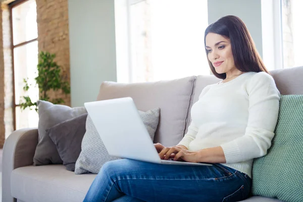 Portrait of her she nice attractive lovely cute cheerful focused girl typing e-mail using laptop sitting on divan in light white interior living-room indoors — Stock fotografie