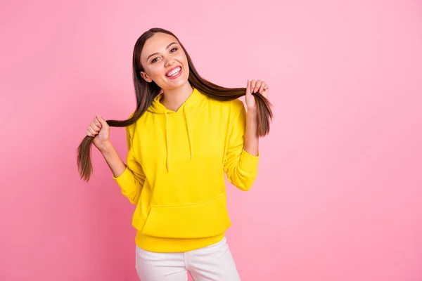 Foto de encantadora linda y atractiva novia sosteniendo su cabello con las manos usando suéter amarillo mientras se aísla sobre el fondo de color pastel rosa — Foto de Stock