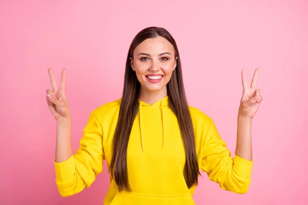 Foto de encantador emocional alegre agradável bonito namorada mostrando-lhe duplo v-sinal sorrindo toothily parecendo ser freelancer vestindo capuz amarelo isolado com fundo de cor pastel rosa — Fotografia de Stock