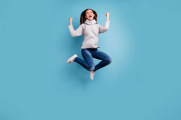 Fotografie exstatický obsah dáma má prázdniny skočit zvednout pěsti jasně oslavovat vítězství obléct bílý moderní vzhled pulovru džínové džíny tenisky izolované přes modrý barevný pozadí — Stock fotografie