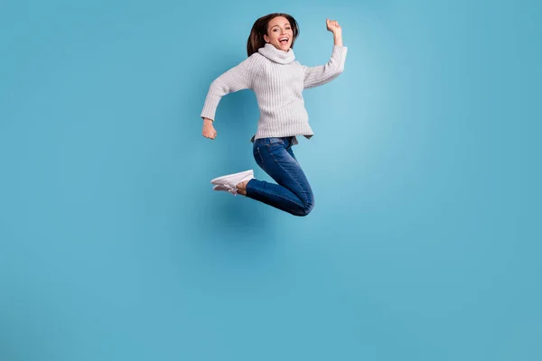 귀여운 흥분 열정적 인 소녀 점프의 전체 길이 사진은 자유 시간을 즐길 수 휴가 착용 흰색 스웨터 풀오버 데님 청바지 운동화 는 파란색 배경 위에 고립 — 스톡 사진