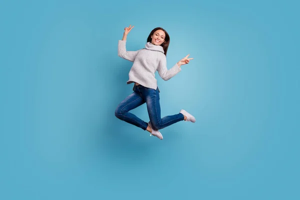 Portret van inhoud speelse Youth Jump hebben vrije tijd maken v-Signs dragen witte gebreide trui Pullover denim jeans sneakers geïsoleerd over blauwe kleur achtergrond — Stockfoto