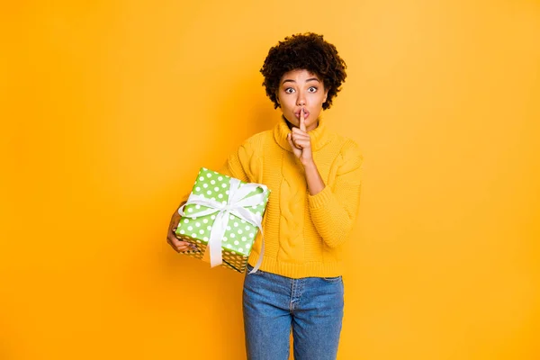 Retrato de ella ella agradable atractivo encantador lindo divertido divertido niña de pelo ondulado sosteniendo en las manos regalo de la cinta de arco mostrando shh signo aislado en brillante brillo vivo vibrante color amarillo fondo — Foto de Stock