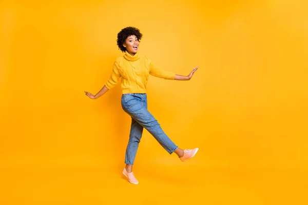 Teljes hosszúságú testméret fotó vidám fekete afro-amerikai nő táncol vagy előrelépni viselt farmer farmer sárga pulóver cipők izolált élénk színű sárga háttérrel — Stock Fotó