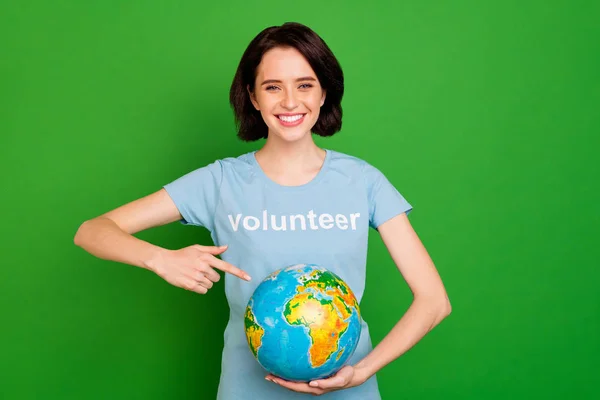 Retrato dela ela agradável atraente linda menina alegre vestindo azul t-shirt segurando as mãos apontando para o globo associação internacional isolado sobre brilhante brilho vívido vibrante fundo verde — Fotografia de Stock