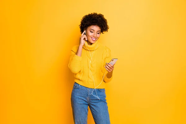 Foto av fina charmiga cutly vågig söt glad fascinerande svart tjej lyssnar på musik med sina hörlurar medan du bär Jeans denim Pullover isolerade över levande färg bakgrund — Stockfoto