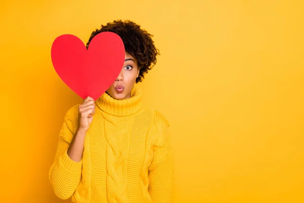 Foto de novia afro de pelo castaño ondulado rizado asomándose desde el gran corazón rojo para besarte a través del aire usando jersey amarillo aislado sobre un fondo de color vibrante —  Fotos de Stock