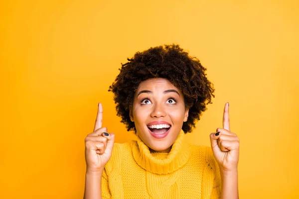 Foto de la mujer bonita de piel oscura que indica los dedos índice hasta el espacio vacío en el cartel fresco usar jersey de punto caliente aislado fondo amarillo — Foto de Stock