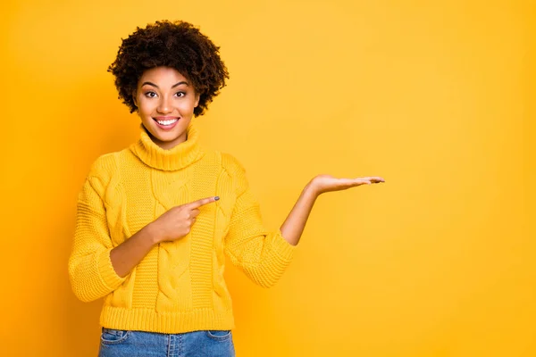 Foto de promotor de mujer de piel bastante oscura sosteniendo en el brazo el mejor producto para el uso final de bajo precio jersey cálido aislado fondo amarillo — Foto de Stock