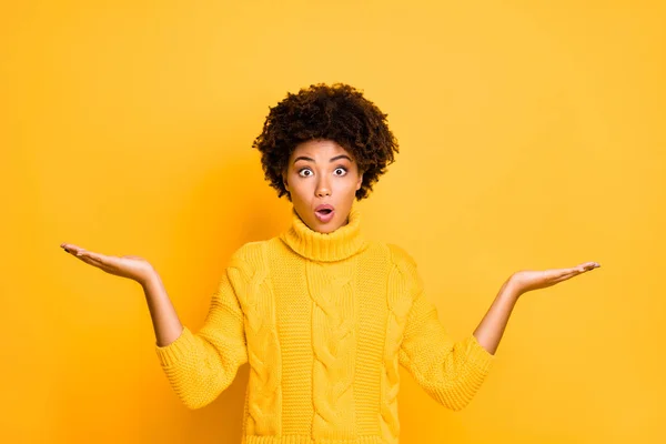 Foto de senhora de pele escura segurando dois novos produtos em braços não acredito que os preços baixos desgaste pulôver de malha isolado fundo amarelo — Fotografia de Stock