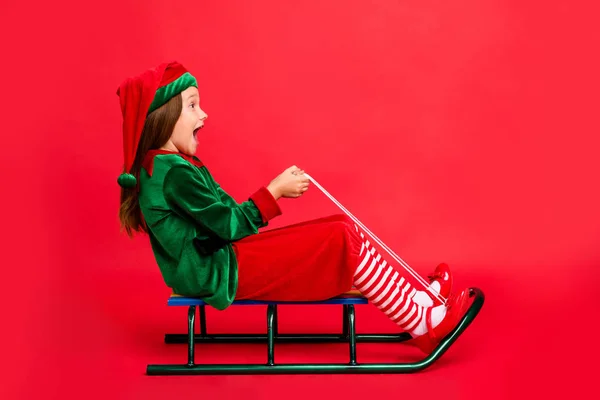 Full längd profilsida foto av upphetsad Elf Kid i hatt med lång röd Head frisyr spann skrikande klädd mössa kostym isolerad över röd bakgrund — Stockfoto