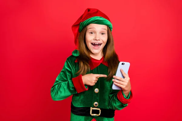 Retrato de elfo sorprendido en el sombrero con el punto rojo largo de la cabeza en su espectáculo de usuario verdadero tecnología moderna como en sus puestos usan gorra de traje verde aislado sobre fondo rojo — Foto de Stock