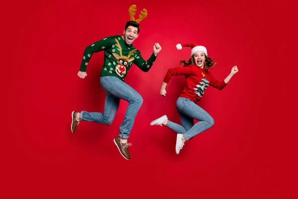 Full length photo of jumping couple excited by x-mas prices hurry buy costumes wear ugly ornament jumpers isolated red color background — ストック写真