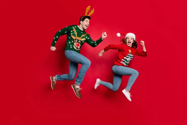 Full body photo of amazed jumping couple excited by x-mas prices hurry shopping wear ugly ornament jumpers isolated red color background — ストック写真