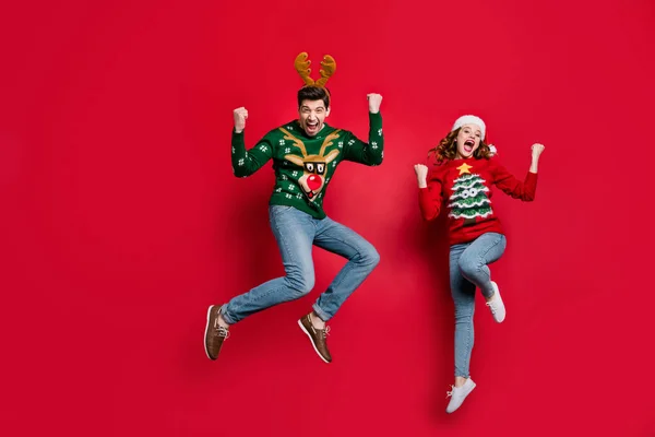 Full length photo of amazed lady and guy jumping excited by x-mas prices wear ugly ornament jumpers and headwear isolated red color background — Stockfoto