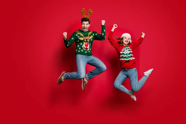 Full size photo of funky lady and guy jumping excited by x-mas prices wear ugly ornament jumpers and headwear isolated red color background — Stok fotoğraf