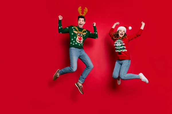 Full längd foto av Lady och Guy hoppning upphetsad av x-mas rabatter bära ful ornament tröjor och huvudbonader isolerad röd färg bakgrund — Stockfoto