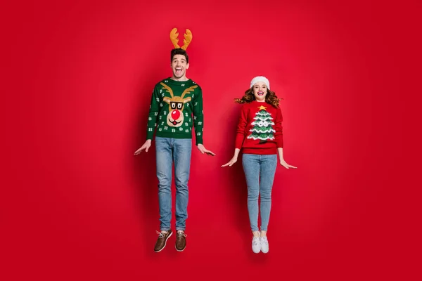 Full body photo of crazy lady and guy jumping high enjoy x-mas sale wear ugly ornament pullovers and headwear isolated red color background — Stockfoto