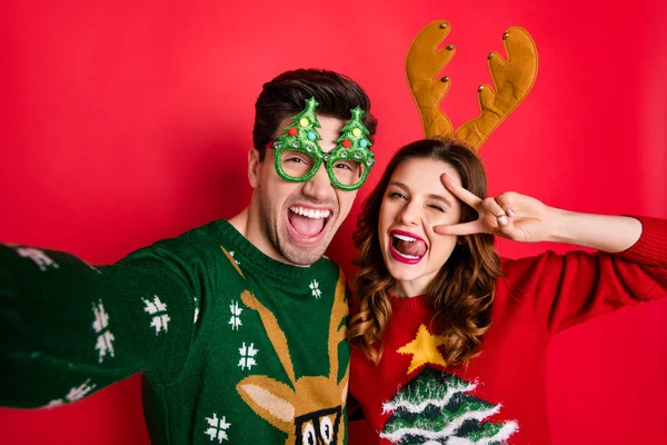 Photo of crazy couple making selfies sticking tongues winking eyes v-signing wear funky ugly ornaments jumpers isolated red color background — Stock Photo, Image