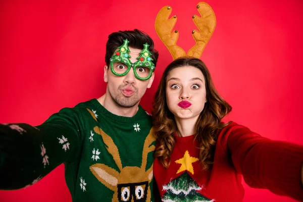 Photo of carefree lady and guy at newyear costume party making selfies with strange faces wear ugly pullovers isolated red color background — Stock Photo, Image