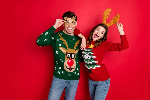 Portrait of funky crazy two people wife husband in brown antlers costume lean shoulder wear denim seasonal clothes christmas tree design pullover jumper spectacles isolated over red color background — Stock Photo, Image